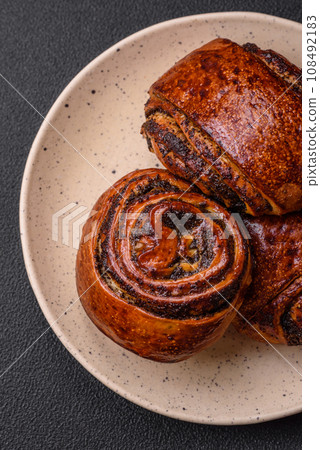 Delicious fresh sweet baked buns with poppy seeds and cinnamon on a ceramic plate Delicious fresh sweet baked buns with poppy seeds and cinnamon on a ceramic plate 108492183
