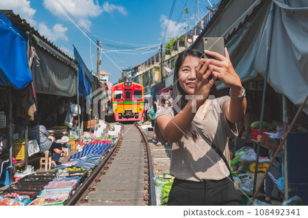 Asian traveler with mobile phone travel at Mae Klong railway market in Thailand 108492341