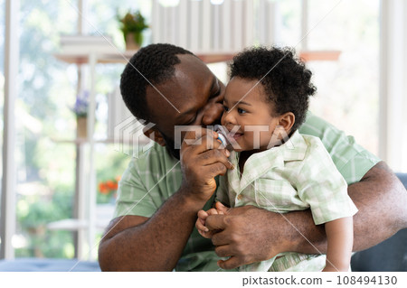 Happy african american man play with little infant toddler child in living room sofa. Parent and little kid relaxing at home. Parents and toddler child girl enjoying spending time at home. Childcare 108494130