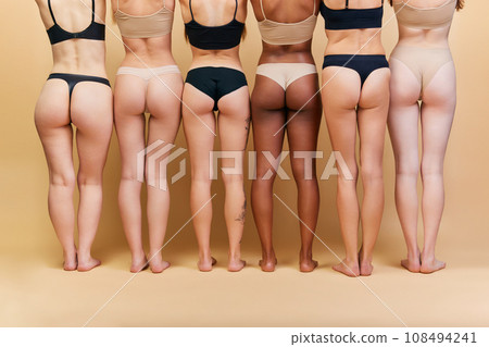 Back view of female bodies of different shapes and skin color standing in underwear against beige studio background. Buttocks and legs Back view of female bodies of different shapes and skin color standing in underwear against beige studio background. Buttocks and legs 108494241