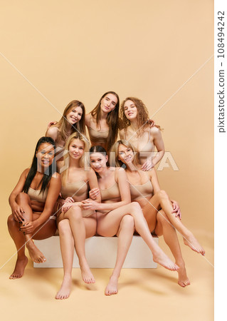 Mixed female beauty. Group of different young women of different age and ethnicity posing in underwear against beige studio background Mixed female beauty. Group of different young women of different age and ethnicity posing in underwear against beige studio background 108494242