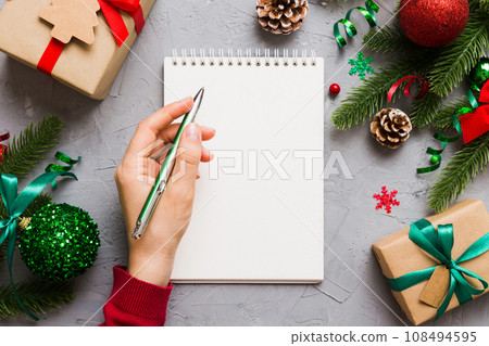 Woman writing Christmas to do list on notebook on colored background with xmas decorations Woman writing Christmas to do list on notebook on colored background with xmas decorations 108494595