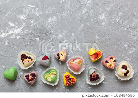 chocolate sweets in the form of a heart with fruits and nuts on a colored background. top view with space for text, holiday concept chocolate sweets in the form of a heart with fruits and nuts on a colored background. top view with space for text, holiday concept 108494596
