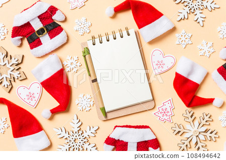 Top view of notebook with Christmas decorations and Santa hats on orange background. Happy holiday concept Top view of notebook with Christmas decorations and Santa hats on orange background. Happy holiday concept 108494642