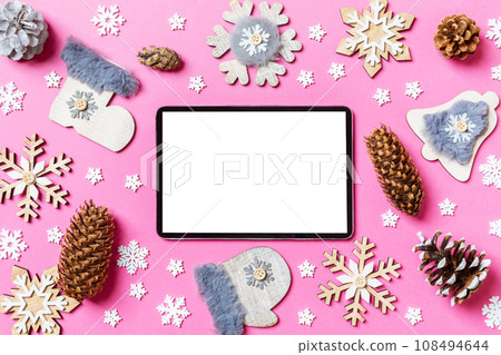 Top view of digital tablet, holiday toys and decorations on pink Christmas background. New Year time concept Top view of digital tablet, holiday toys and decorations on pink Christmas background. New Year time concept 108494644