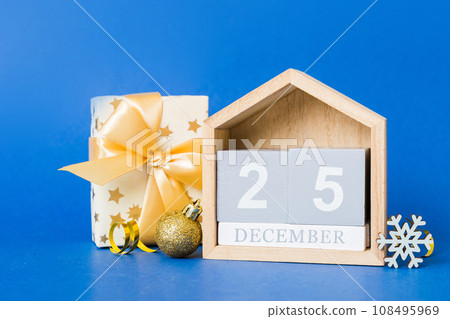25 december. Christmas composition on colored background with a wooden calendar, with a gift box, toys, bauble copy space 108495969