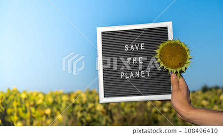 Unrecognizable person with banner message SAVE THE PLANET in sunflower field on sunny day. Sign EARTH day. Concept of ecology and eco activism environmental issues Stop global warming. Go green 108496410