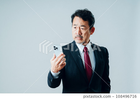 A senior man operating a smartphone. (gray background) A senior man operating a smartphone. (gray background) 108496716