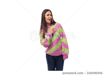 stylish cheerful young brunette woman in a striped pink sweater points her finger to the side on a 108496948