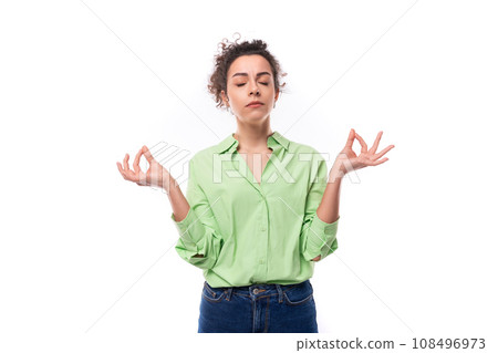 stylish young brunette curly woman with a ponytail hairstyle dressed in a green shirt is meditating 108496973