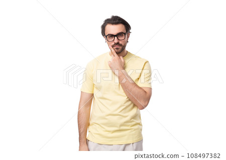 a young European brunette guy with a beard and mustache in glasses stands thoughtfully on a white a young European brunette guy with a beard and mustache in glasses stands thoughtfully on a white 108497382