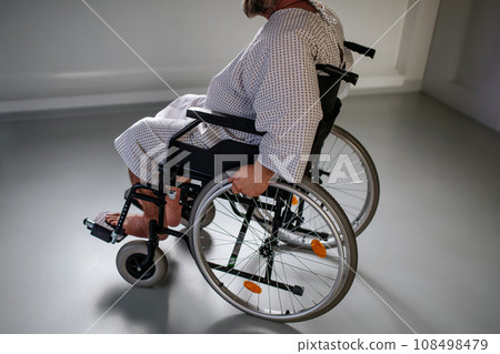Side view of man in wheelchair. Overweight patient in hospital gown waiting for medical examination in hospital. 108498479