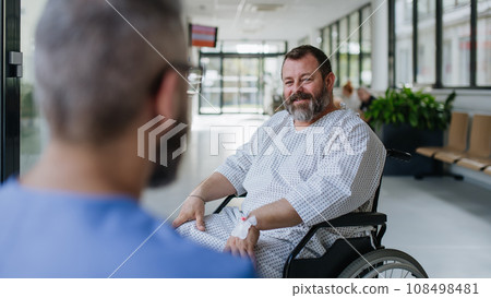 Close up of supportive doctor talking with worried overweight patient in wheelchair. Illnesses and diseases in middle-aged men's health. Compassionate physician supporting stressed patient. Concept of 108498481