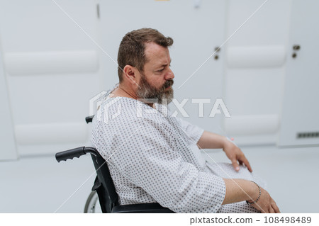 Side view of man in wheelchair. Overweight patient in hospital gown waiting for medical examination in hospital, feeling anxious. 108498489