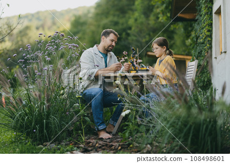 Father supporting daughter in pursuing robotics, science, IT technologies and programming. Young girl assembling a simple robot and her dad helping her. 108498601