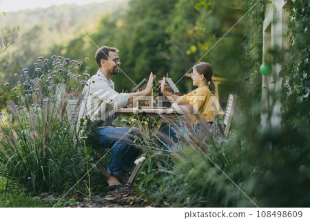 Father with daughter making bug hotel, or insect house outdoors in the garden. Girl learning about insects, garden ecosystem and biodiversity. Girl and dad high five each other. 108498609