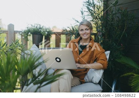 Woman working in the garden, with laptop on legs. Businesswoman working remotely from outdoor homeoffice, thinking about new business or creative idea. Concept of outdoor home office. 108498622