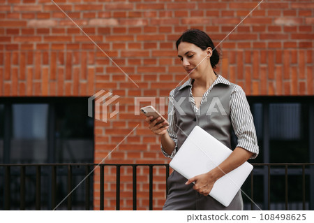 Beautiful woman in business attire standing on city street. Muslim businesswoman with laptop making call. Iran, Female university professor in front of university building. Beautiful woman in business attire standing on city street. Muslim businesswoman with laptop making call. Iran, Female university professor in front of university building. 108498625