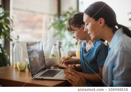 Mom and daughter watching entertaining videos on mom's work laptop. Remote work, home office for mothers with children. 108498638