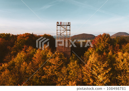 Aerial view of a wooden lookout tower in autumn nature. People stand on the observation tower, enjoying the beautiful, serene view of the surrounding landscape. 108498781