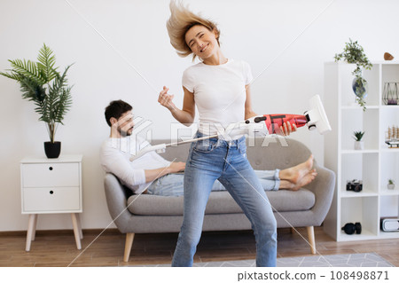 Woman dancing with cordless vacuum while man using laptop 108498871