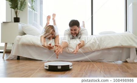 Family husband and wife on bed playing with cleaning robot 108498986