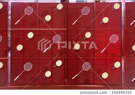 Table tennis and badminton rackets are hung on a red square grill steel grid, used as a backdrop for various events. 108499193