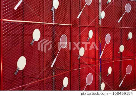 Table tennis and badminton rackets are hung on a red square grill steel grid, used as a backdrop for various events. 108499194