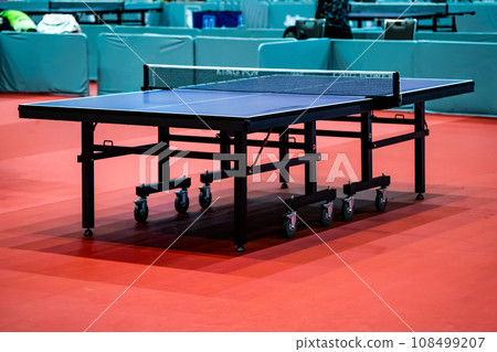 Blue table tennis or pingpong table is settle on a red, orange floor of the indoor court stadium for competitions tournament. 108499207