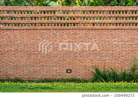 The brick wall, fence barrier is designed with a hole on top of wall in Asian style with garden grass field in the foreground 108499255