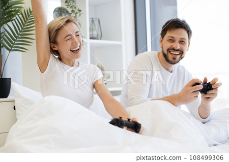Front view of caucasian playing video games while sitting under blanket at home. Front view of caucasian playing video games while sitting under blanket at home. 108499306