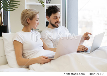 Loving couple resting together in bed and using laptops 108499435