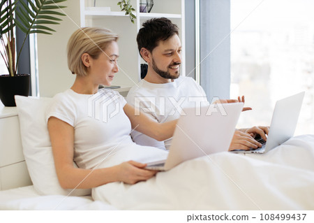 Loving couple resting together in bed and using laptops 108499437