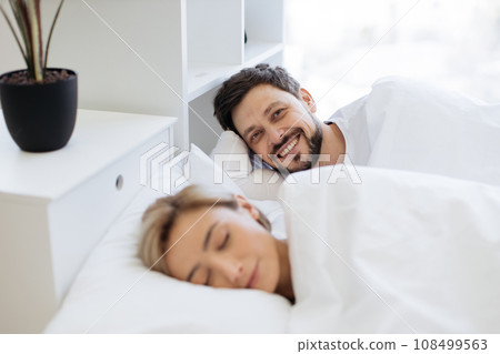 Man smiling on camera while woman sleeping in bed 108499563