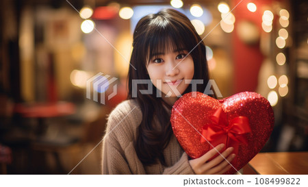 Cute girl smiling while holding a Valentine's gift in both hands 108499822