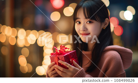 Cute girl smiling while holding a Valentine's gift in both hands 108499826
