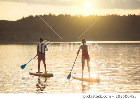 Man and woman sup board surfers at sunset. 108500453