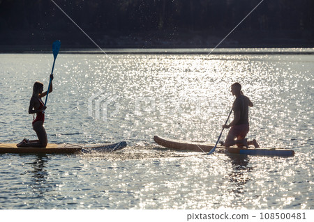 Happy couple man and woman floats on river on supboards sunset. Happy couple man and woman floats on river on supboards sunset. 108500481