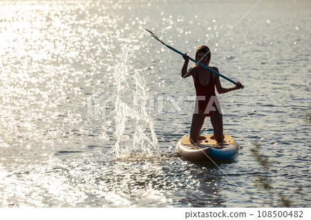 Woman paddling supboard in the sea at sunset. Woman paddling supboard in the sea at sunset. 108500482