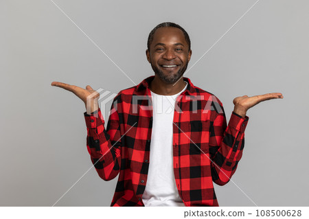 Joyful black bearded man wearing red checkered shirt presenting copy space on palms Joyful black bearded man wearing red checkered shirt presenting copy space on palms 108500628