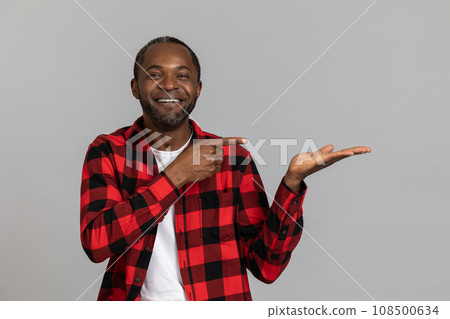 Happy black bearded man wearing red checkered shirt pointing at advertisement area on palm 108500634