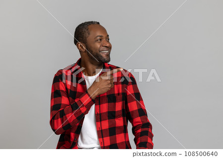 Positive black bearded man wearing red checkered shirt pointing at advertisement area 108500640