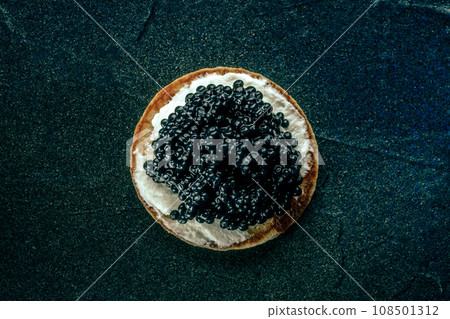 A blini with caviar and cream cheese, overhead flat lay shot on black A blini with caviar and cream cheese, overhead flat lay shot on black 108501312