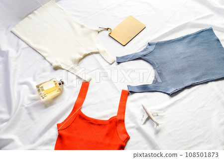On the white sheet were three tank tops, red, white and blue, interspersed with perfume, model and notebook. 108501873