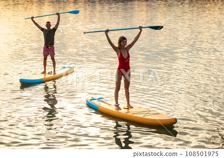 Male and female during paddleboarding at sunset. 108501975