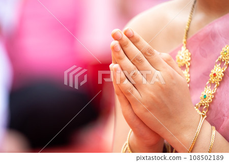 A Lady clasps her hands in front of her chest to pray. She wears .Thai traditional costume in Pink with golden traditional accessories, necklace and bracelets. . A Lady clasps her hands in front of her chest to pray. She wears .Thai traditional costume in Pink with golden traditional accessories, necklace and bracelets. . 108502189
