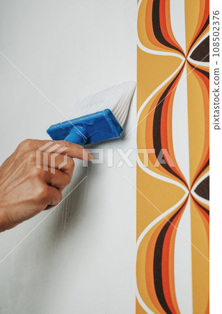 man applying glue to the wall with a pasting brush 108502376