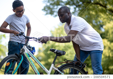 Dark-skinned man fixing a bike in the park 108504571