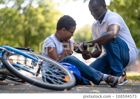 Dad helping his son after falling down from a bike 108504573
