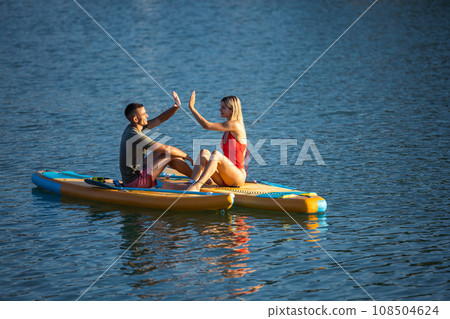 Young woman and sitting on sup board in the open ocean. Young woman and sitting on sup board in the open ocean. 108504624